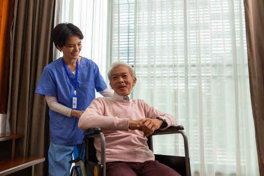 Friendly Staff Caregiver Of Nursing Home Talking To Asian Senior Man In Living Room