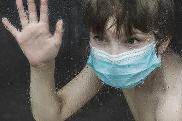 Covid 19 pandemic toll on kids boy with mask looking through window sadly