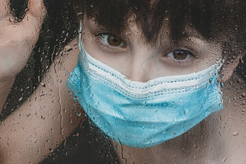 Covid 19 pandemic toll on kids boy with mask looking through window sadly