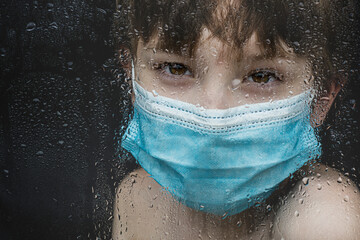 Covid 19 pandemic toll on kids boy with mask looking through window sadly