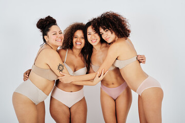 Cheerful diverse women in underwear hugging in studio