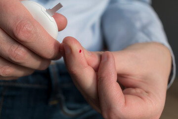 Fototapeta premium Woman pricking her finger to check blood glucose level with glucometer, test blood glucose for diabetes