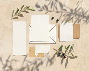 Blank cards on concrete table with olive tree branches and hard shadows, wedding mockup