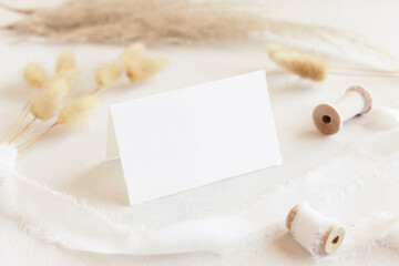 Folded card near silk ribbons and dried hare's tail grass close up on white, boho mockup