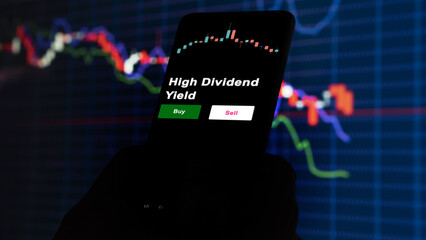 An investor's analyzing the High Dividend Yield etf fund on screen. A phone shows the ETF's prices high dividend yield to invest
