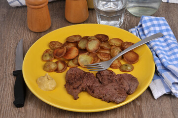 Steak de bœuf avec des pommes de terre rissolée et de la moutarde servis dans une assiette avec une fourchette