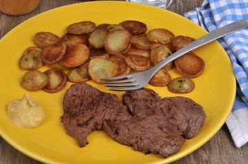 Steak de bœuf avec des pommes de terre rissolée et de la moutarde servis dans une assiette avec une fourchette
