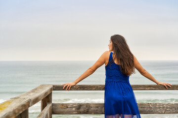 a young woman leaning on the beach boardwalk looking at the misty ocean