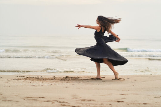 a dancer in a black dress on the beach expressing strength and courage in her movements