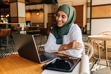 Happy Muslim student having a video call in a cafe