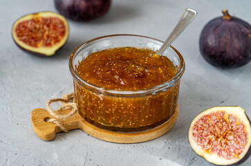 Fig jam in a glass jar with fresh fruits on gray concrete background. Close up