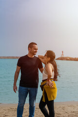 Couple of man and woman dressed casually standing on the beach looking at each other with the sea and sky in the background