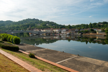 Looking across the placid River Lot towards St-Sylvestre-sur-Lot town and historic hilltop Penne d'Agenais, Lot-et-Garonne, France from the riverside at Port de Penne.
