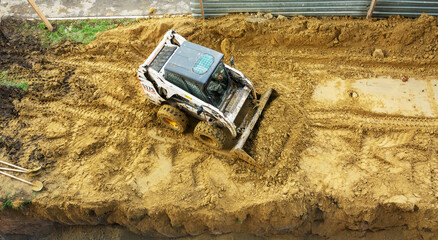 A small tractor works in the sand, filling up a hole.View from above. - obrazy, fototapety, plakaty