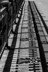 Details of the city's architecture - a symmetrical shadow on the asphalt from a heavy forged fence, black and white photo