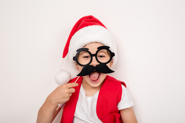 A boy with paper glasses in red Santa Claus hat isolated on white background. Portrait of little 5 year happy beautiful smiling european child in New Year masquerade costume and photo props accessory