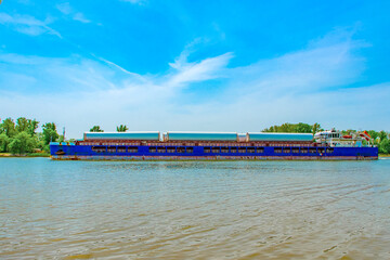 A large cargo ship is sailing on the river. The ship is carrying cargo