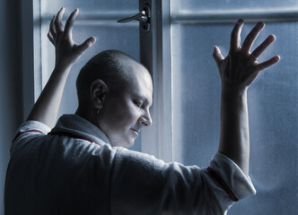 Middle aged bald woman cancer patient standing in front of hospital window