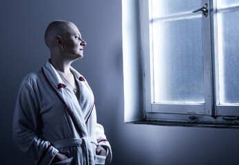 Middle aged bald woman cancer patient standing in front of hospital window