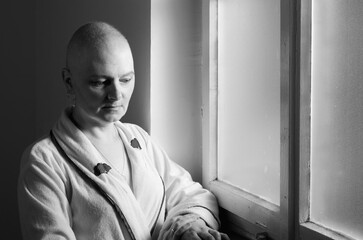 Middle aged bald woman cancer patient standing in front of hospital window