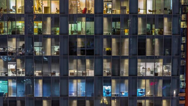 Night aerial view of office building glass window facade with illuminated lighted workspace rooms timelapse. Glowing and flashing light in skyscraper