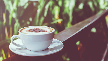 Hot coffee in white cup on weeden fence in the garden. vintage style effect picture