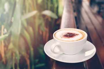 Hot coffee in white cup on weeden fence in the garden.