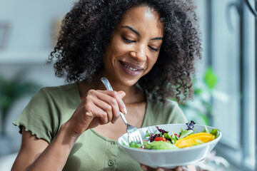 Beautiful woman eating healthy salad while sitting on couch at home.