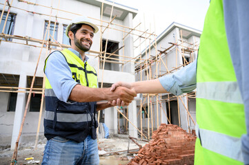 Construction engineer and architect with blueprint shaking hands while standing on construction site. Home building and Work success concept.