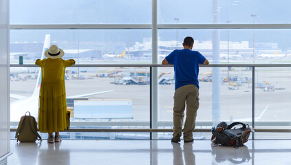 Back view of tourist standing near window at the international airport terminal with backpacker on...
