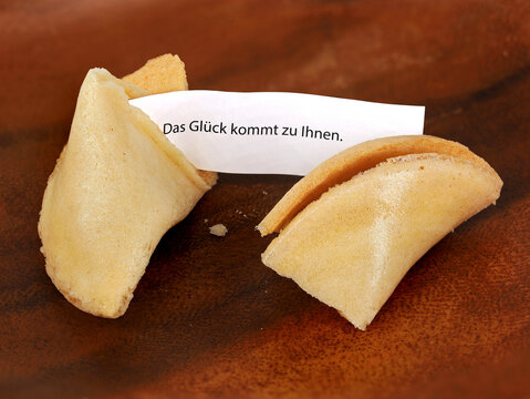 broken chinese fortune cookie with german words saying, luck comes to you, on wooden mahagoni background