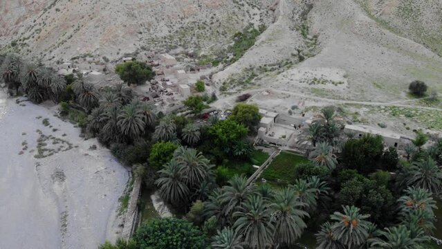 Aerial View Of Village Located In Khuzdar With Lush Green Trees And Gardens Surrounded By Desert Landscape. Dolly Back, Ascending Shot