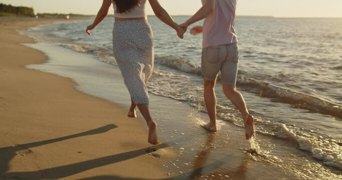 Young loving couple spend time on the beach at sunset. Man and woman have fun running on the beach holding hands. Travel vacation lifestyle.