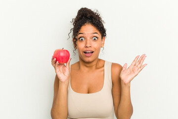 Young brazilian woman holding a red apple isolated receiving a pleasant surprise, excited and raising hands.