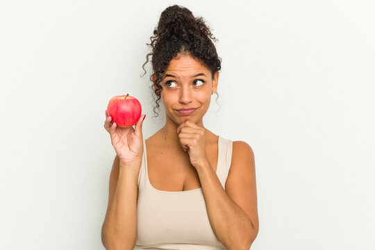 Young brazilian woman holding a red apple isolated looking sideways with doubtful and skeptical expression.