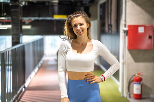 Smiling young sporty woman wearing sportswear and standing at the gym. Fitness woman taking a break in a gym with a hand on a hip.