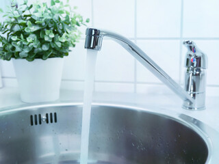 A stream of clean water drink flows from the kitchen faucet into the stainless steel sink....