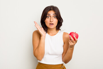 Young Indian woman holding an apple isolated on white background surprised and shocked.