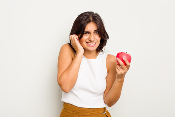 Young Indian woman holding an apple isolated on white background covering ears with hands.