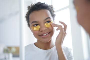 Pretty mixed race girl applying moisturizing golden under eye patches. Skincare, beauty routine