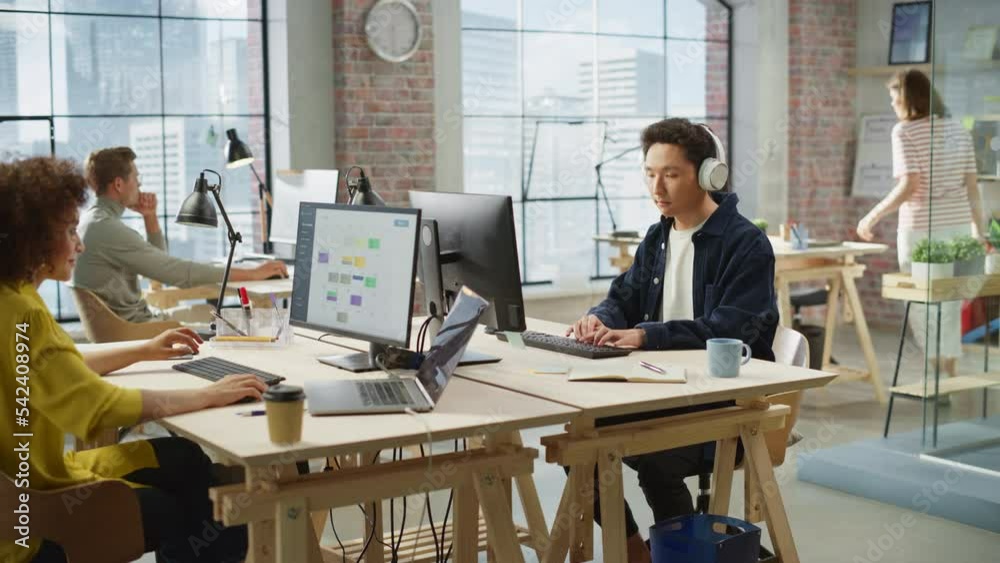 Poster Multiethnic Creative Colleagues Working Using Computers in an Open Office During Day Time. Asian Man Listening to a Meeting on Headphones. Female Director working on a Schedule. Handheld Shot.
