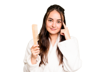 Young caucasian woman holding a hairbrush isolated on green chroma background pointing temple with finger, thinking, focused on a task.