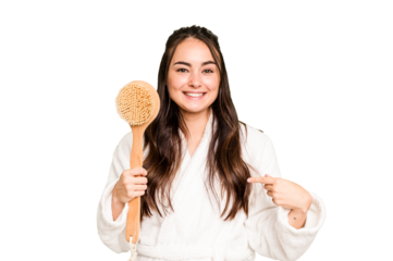 Young caucasian woman holding shower brush isolated on green chroma background person pointing by hand to a shirt copy space, proud and confident