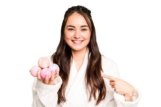 Young caucasian woman holding aromatic balls for bathtub isolated on green chroma background person pointing by hand to a shirt copy space, proud and confident