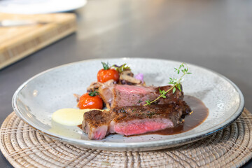 Medium Rare Beef Steak was grilled and fried with sliced mushroom and mini tomato on white dish, ready to serve and eat.
