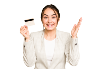 Young caucasian woman holding a credit card isolated on green chroma background receiving a pleasant surprise, excited and raising hands.