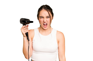 Young caucasian woman holding a hairdryer on green chroma background screaming very angry and...