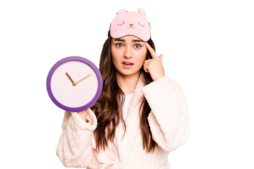 Young caucasian woman holding a clock wearing a pajama isolated on green chroma background showing a disappointment gesture with forefinger.