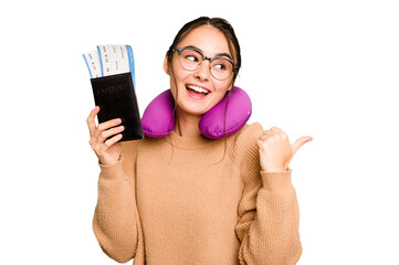 Young caucasian woman with inflatable travel pillow holding passport isolated on green chroma background points with thumb finger away, laughing and carefree. © Asier