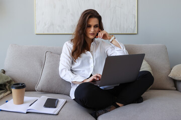 Young woman sitting on the couch and working on a laptop at home